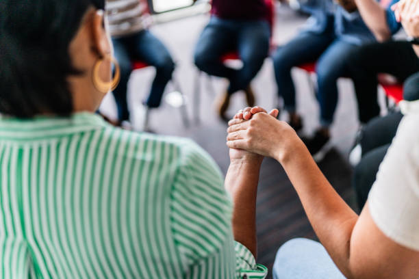 Two people holding hands in support during a group meeting